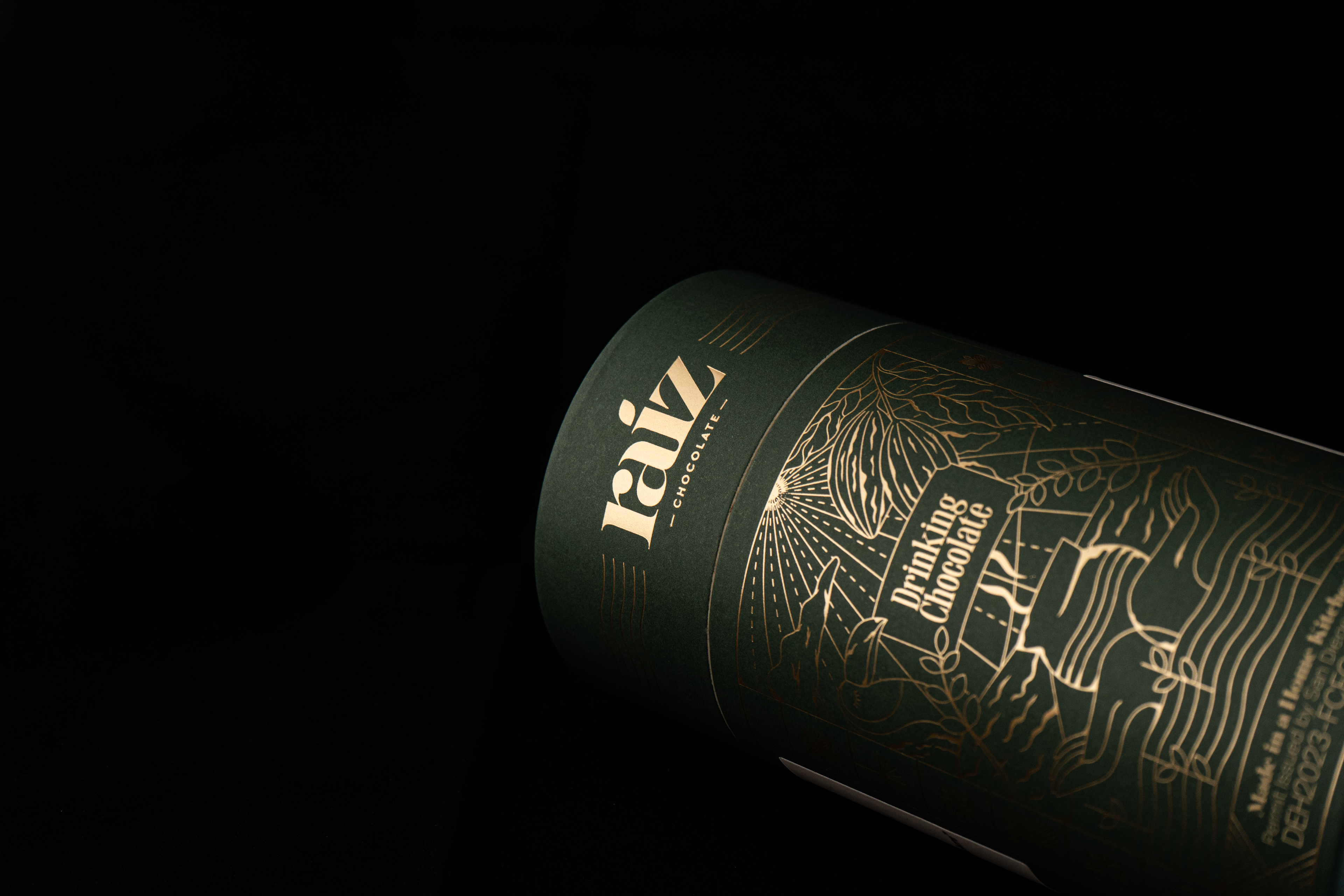 Drinking Chocolate tube packaging with gold text and illustrations on a black background