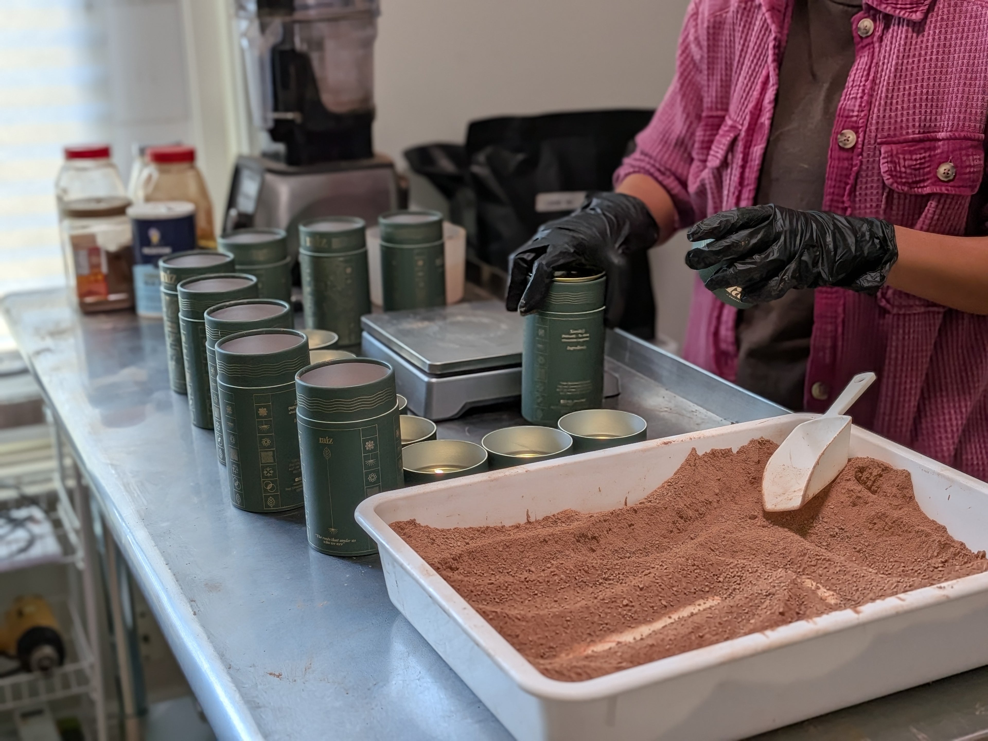 Person handling containers on a counter with a tray of powdered chocolate.
